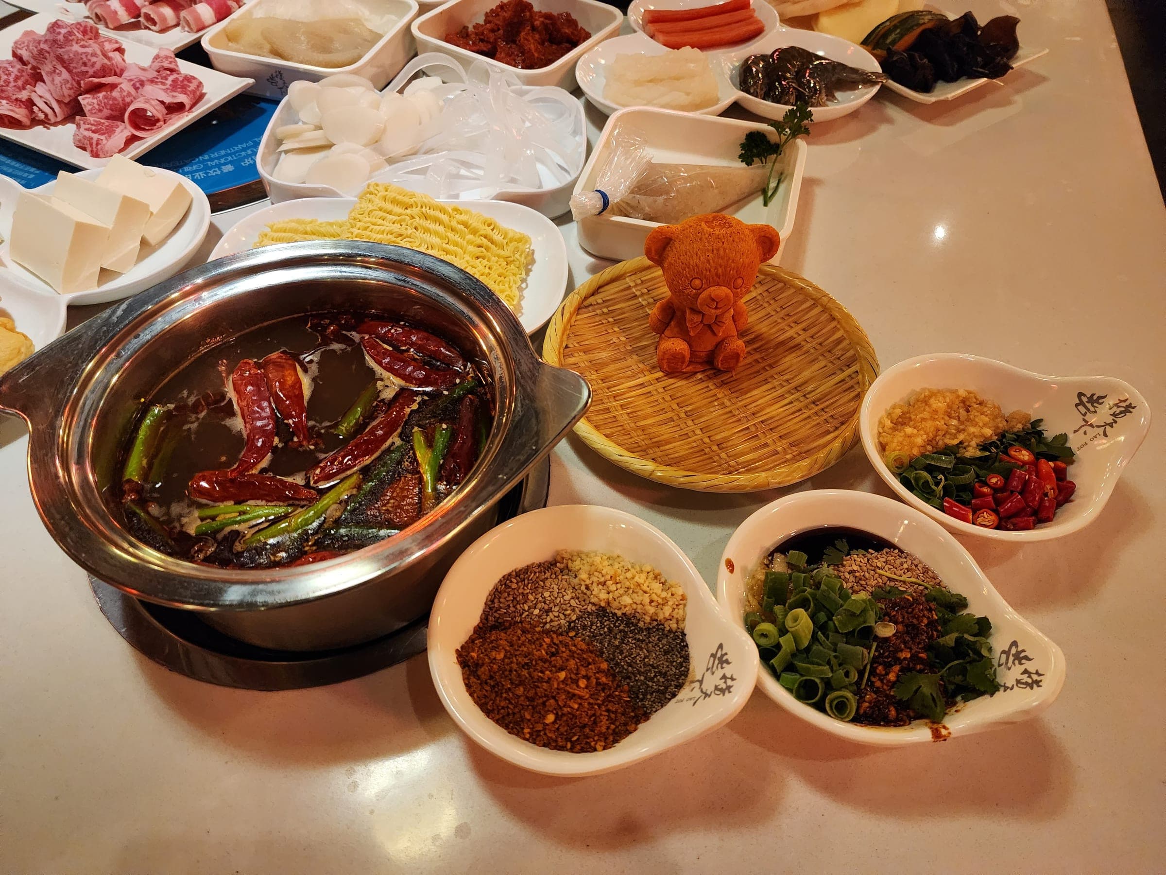 A pot of red spicy tallow broth full of dried chilies next to a bear-shaped block of tallow broth base on a bamboo tray.