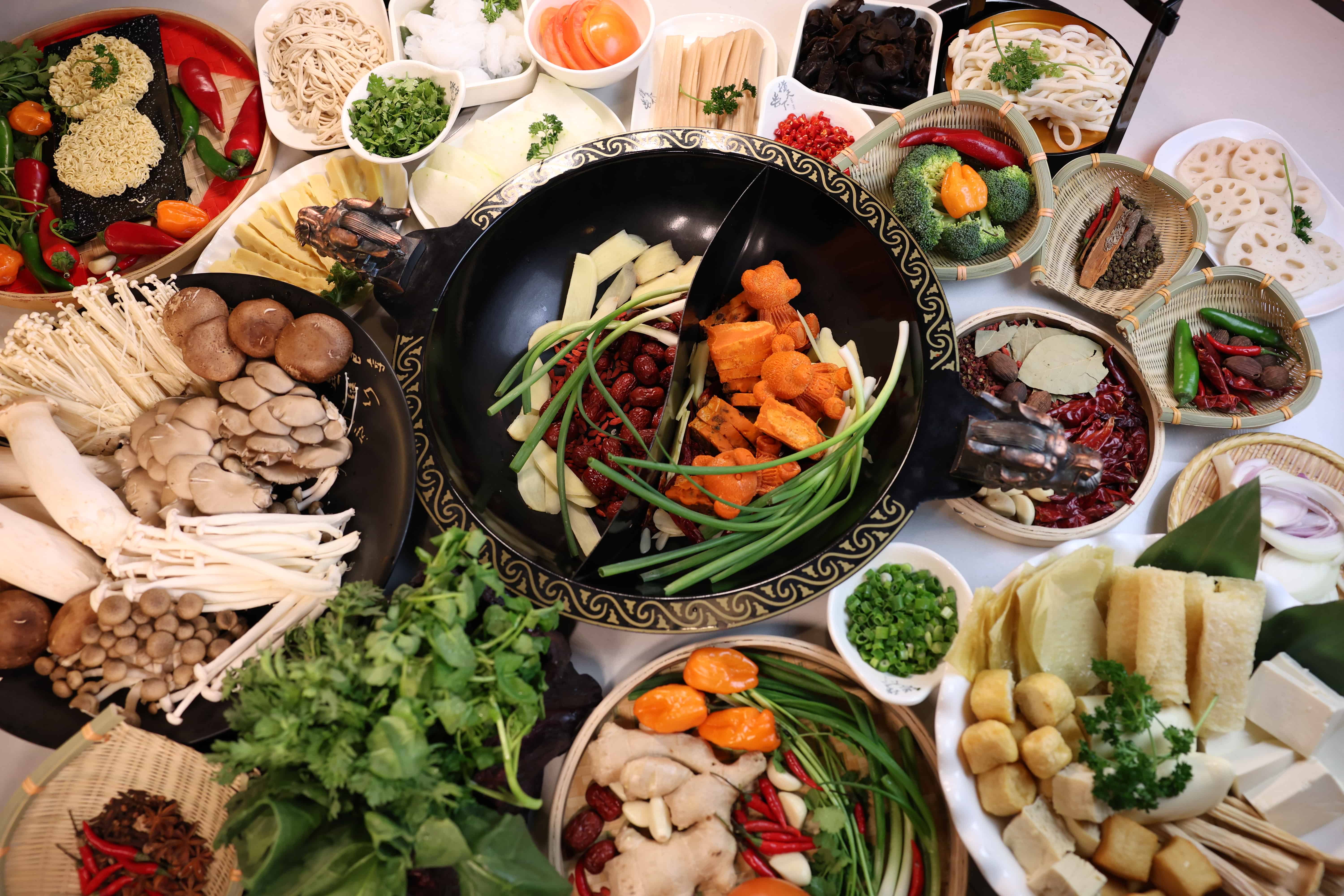 A nice pot stewing up some hotpot with ingredients around it.